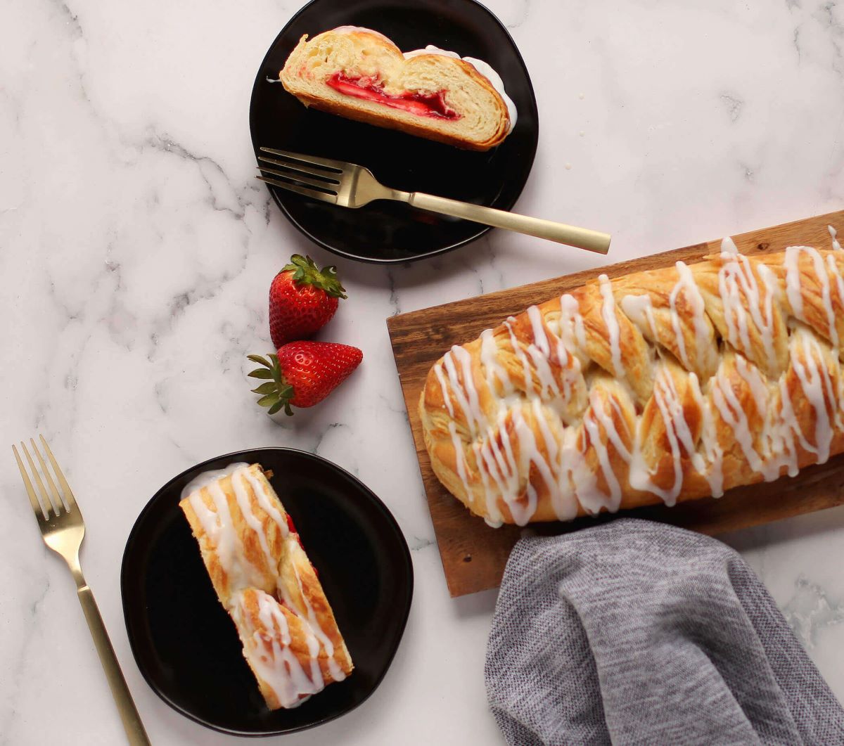 Strawberry Cream Cheese Butter Braid Pastry next to two plates with slices of pastry, forks, and strawberries